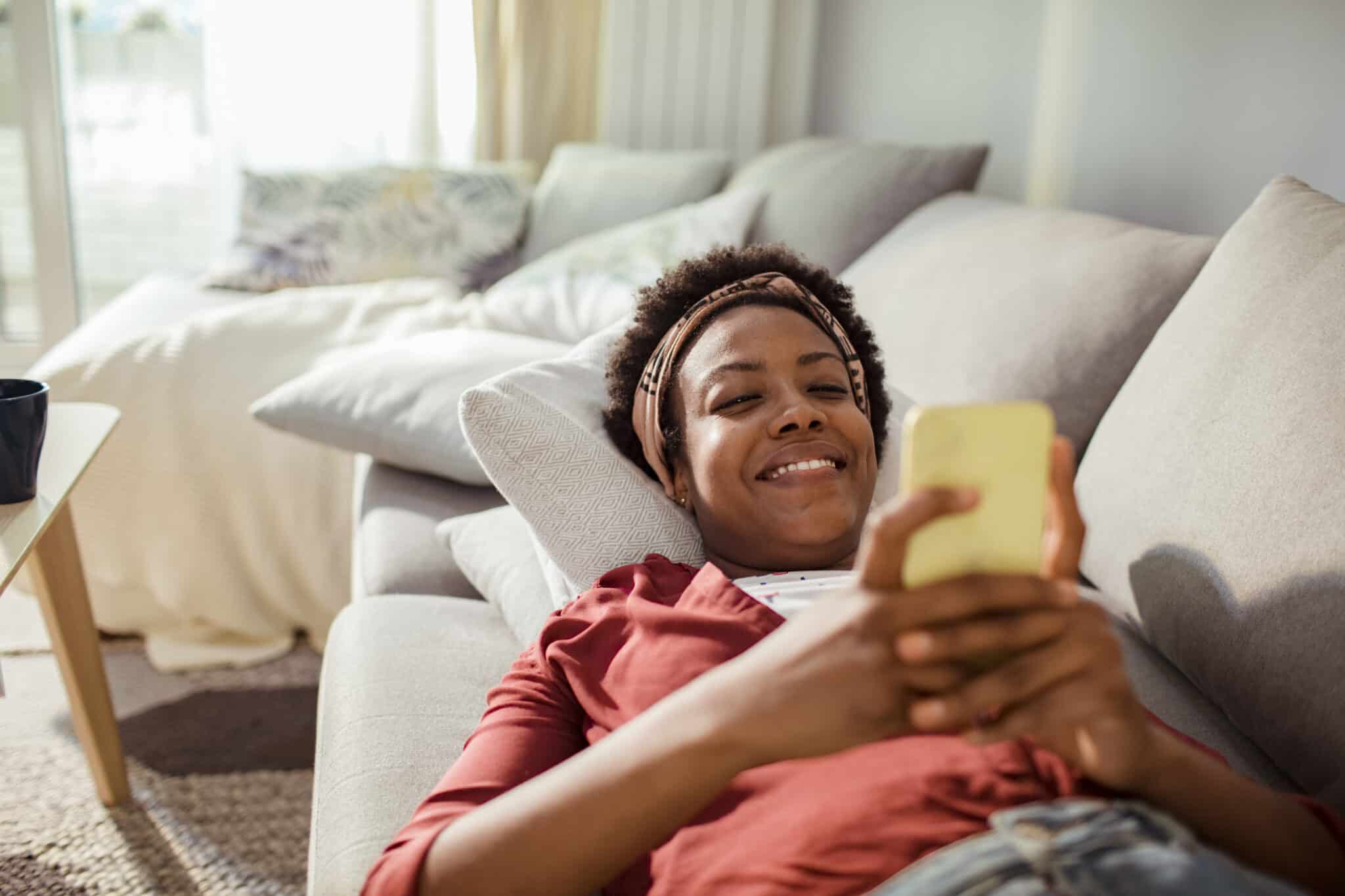 Smiling woman relaxing on a couch while banking on her phone